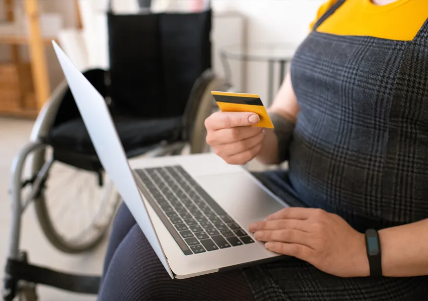 Close-up of unrecognisable disabled woman using laptop while paying with credit card online
