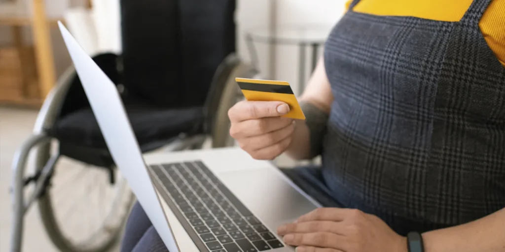 Close-up of unrecognisable disabled woman using laptop while paying with credit card online